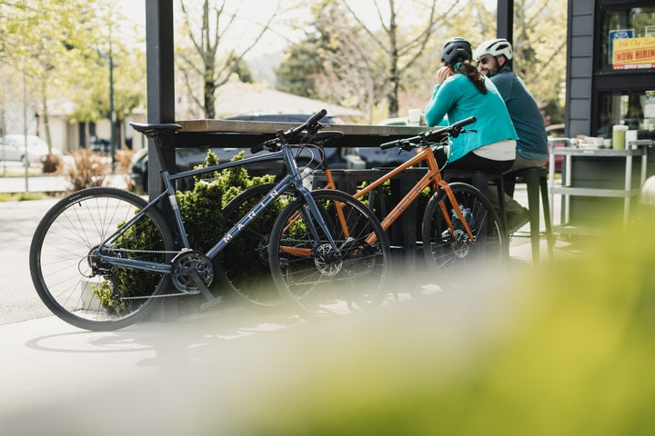 two people sat on a bench with bikes leaning against an outside bar 