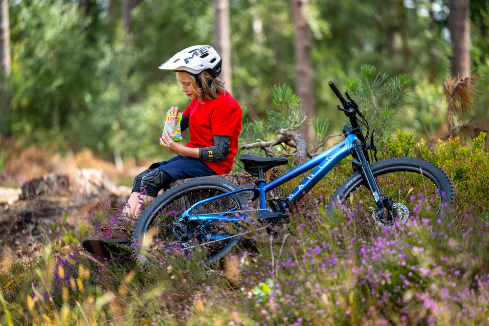 kid sits on rock and eats candy with bike in foreground