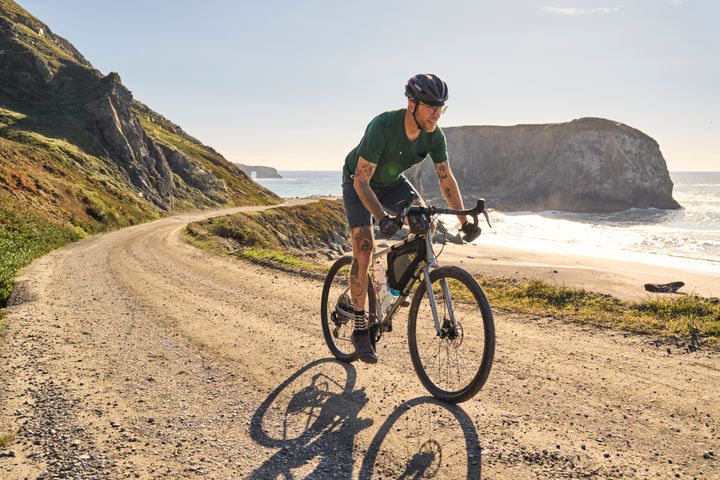 man riding his bike by the sea on a gravel path