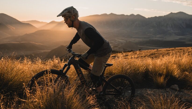 An image of a male mountain bike rider riding a Marin Bikes Alpine Trail E at golden hour with large mountains in the background