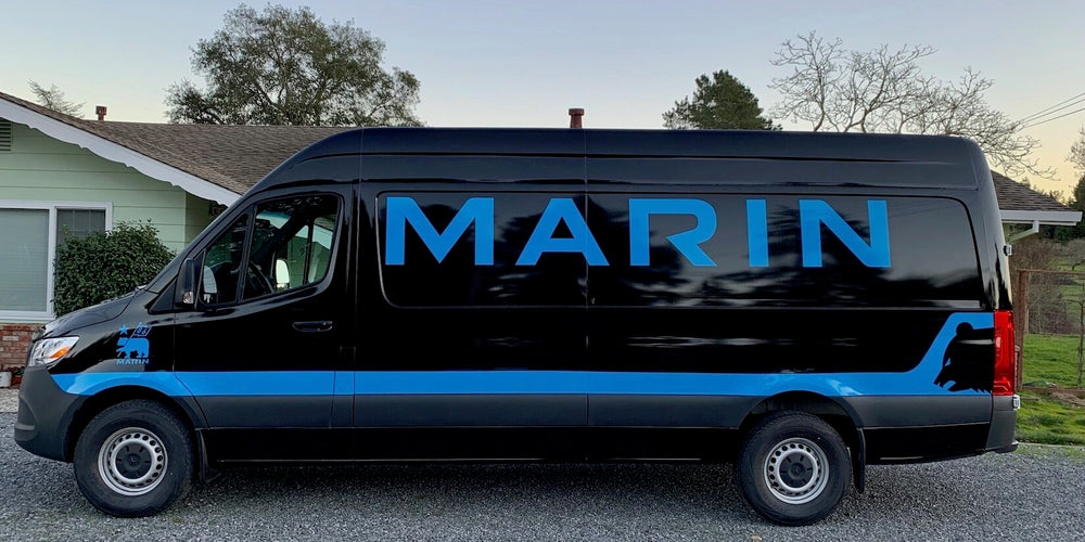 An image of a black and blue Marin Bikes Mercedes Sprinter van parked outside a house