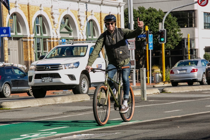 Man riding a bicycle on a city street with buildings and cars in the background