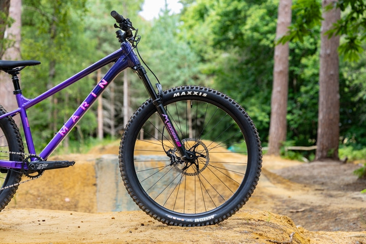 Purple mountain bike with Maxxis tires on a wooden platform in a forest setting