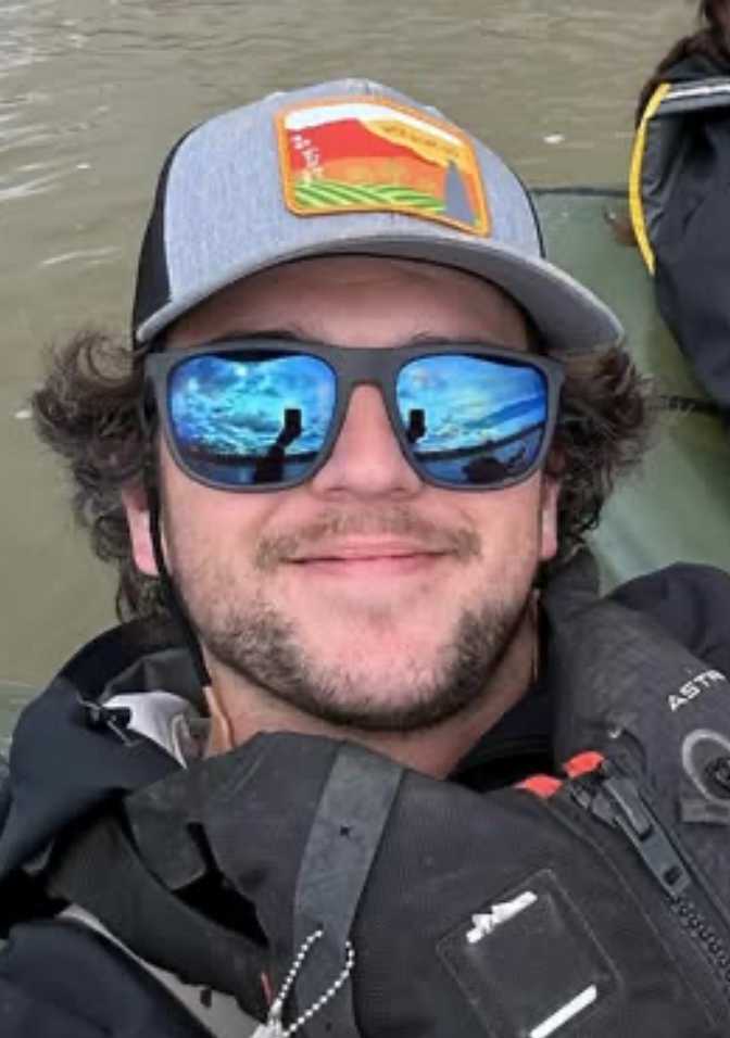 Man wearing sunglasses and a cap with a reflection of water and sky.