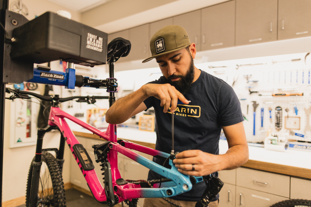 Person working on a pink and blue bicycle in a workshop setting